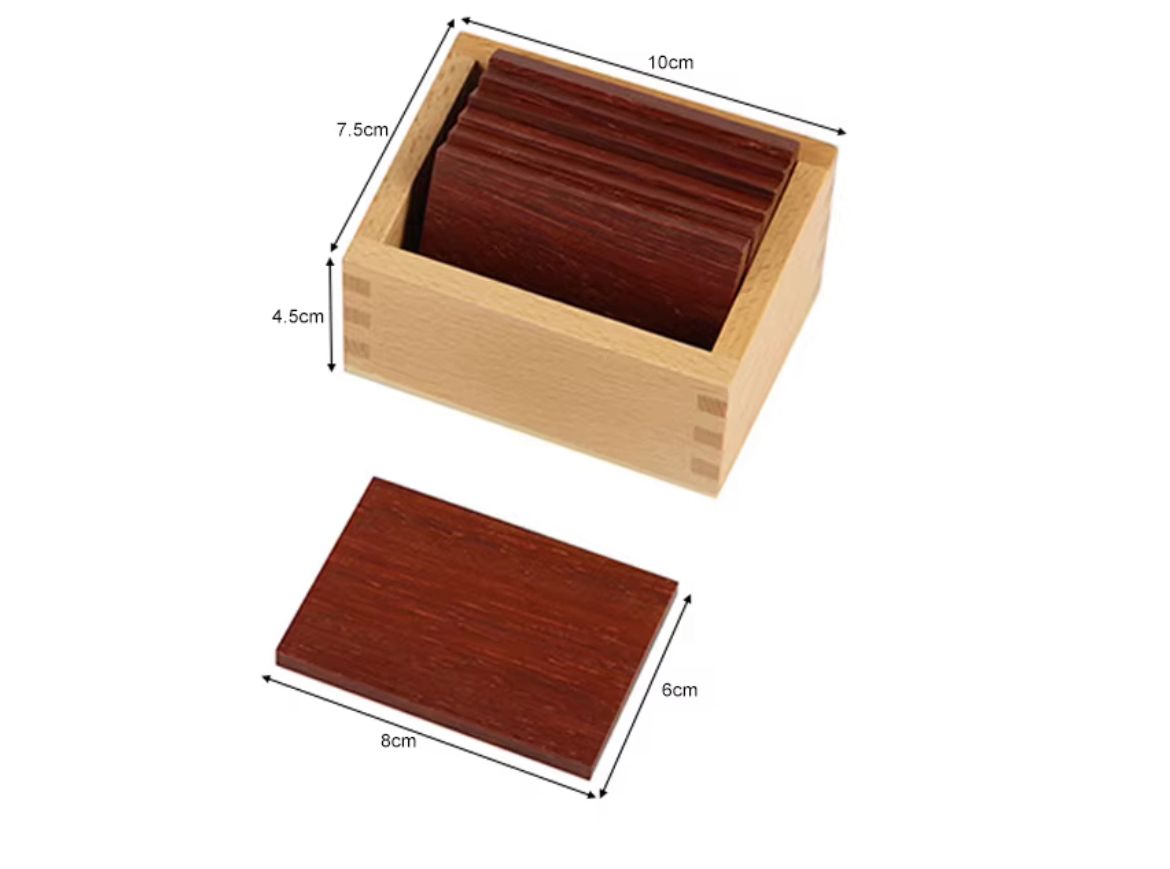 Dark wooden Montessori baric tablets inside a wooden storage box with labeled size measurements for tactile and pressure discrimination learning.