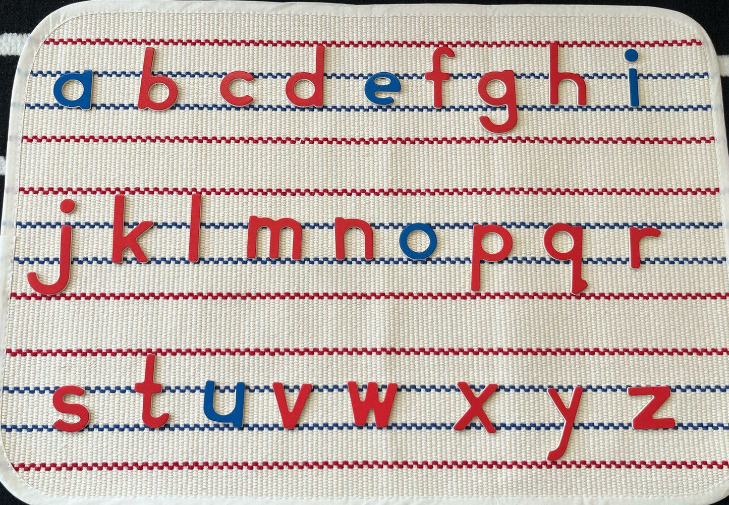 Montessori movable alphabet rug with red and blue lowercase letters arranged on lined mat for language learning