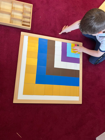 Top view of colorful nested square puzzle pieces arranged on a wooden Montessori board.