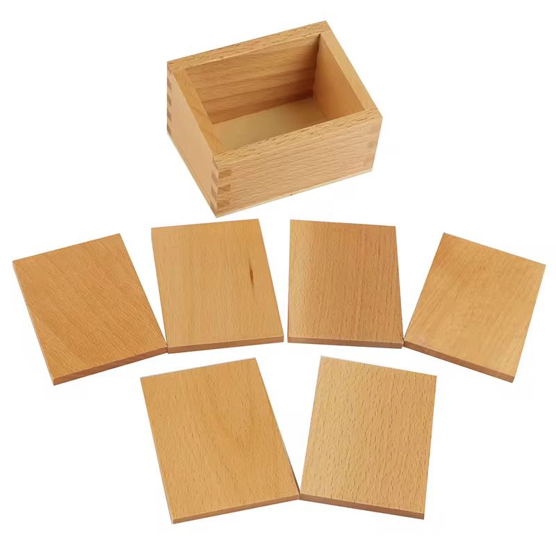 Light wooden Montessori baric tablets arranged in front of a wooden storage box for pressure and weight discrimination activities.