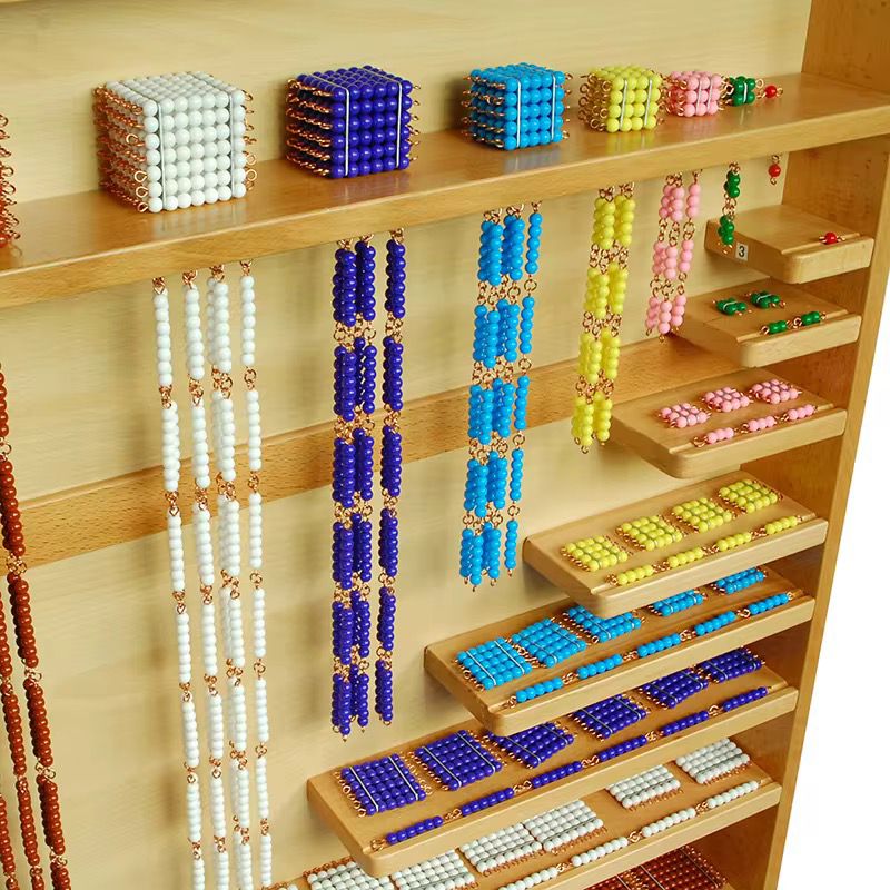 Close-up view of Montessori bead materials showing bead bars, bead squares, and bead cubes in various colors organized on stepped wooden shelves.
