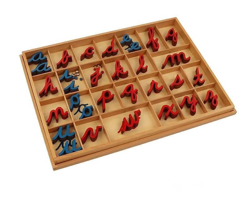 Montessori cursive movable alphabet letters arranged inside a wooden tray with separated compartments.