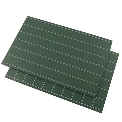 Two green Montessori double-sided chalkboards stacked together, showing writing lines and square grids for early handwriting practice.