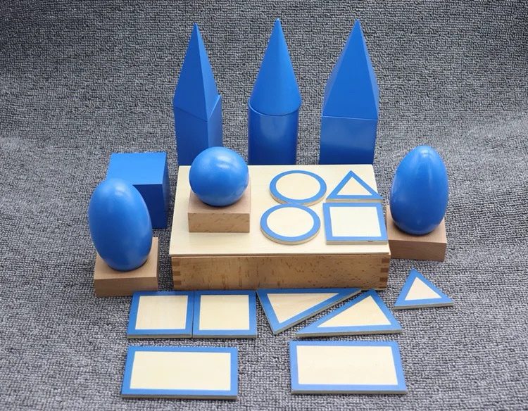 Montessori geometric solids set with blue 3D shapes, wooden bases, and matching 2D shape cards arranged on a table.
