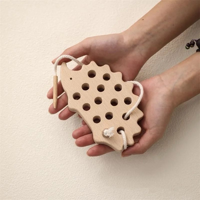 Toddler holding wooden hedgehog lacing toy to practice fine motor and hand control skills