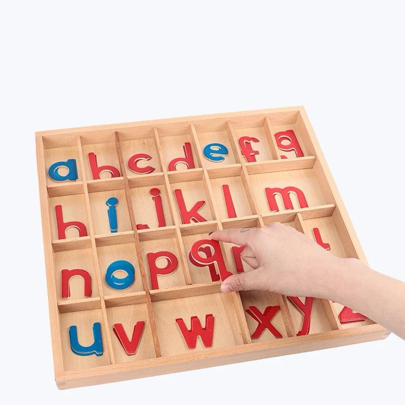 A child’s hand selecting a lowercase letter from a wooden Montessori movable alphabet box containing red consonants and blue vowels.