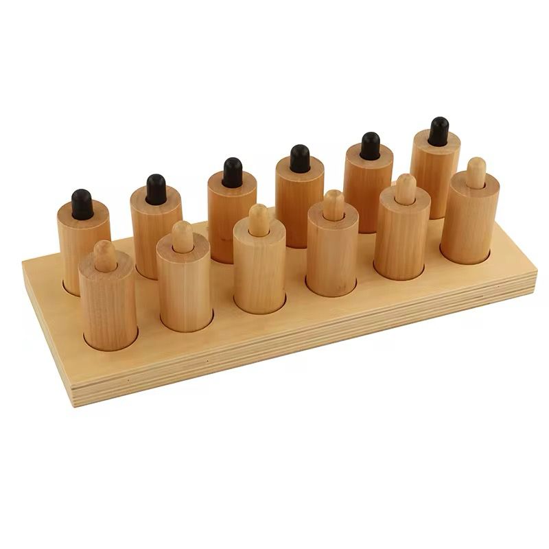 Montessori pressure cylinders arranged on wooden board for sensory discrimination activity