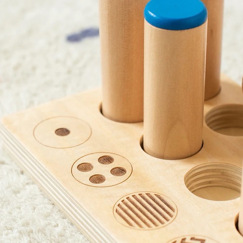 Close-up of wooden Montessori sound cylinders showing engraved pattern symbols on the base tray