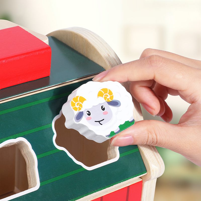 Hand inserting sheep shape into wooden farm toy roof slot for shape matching