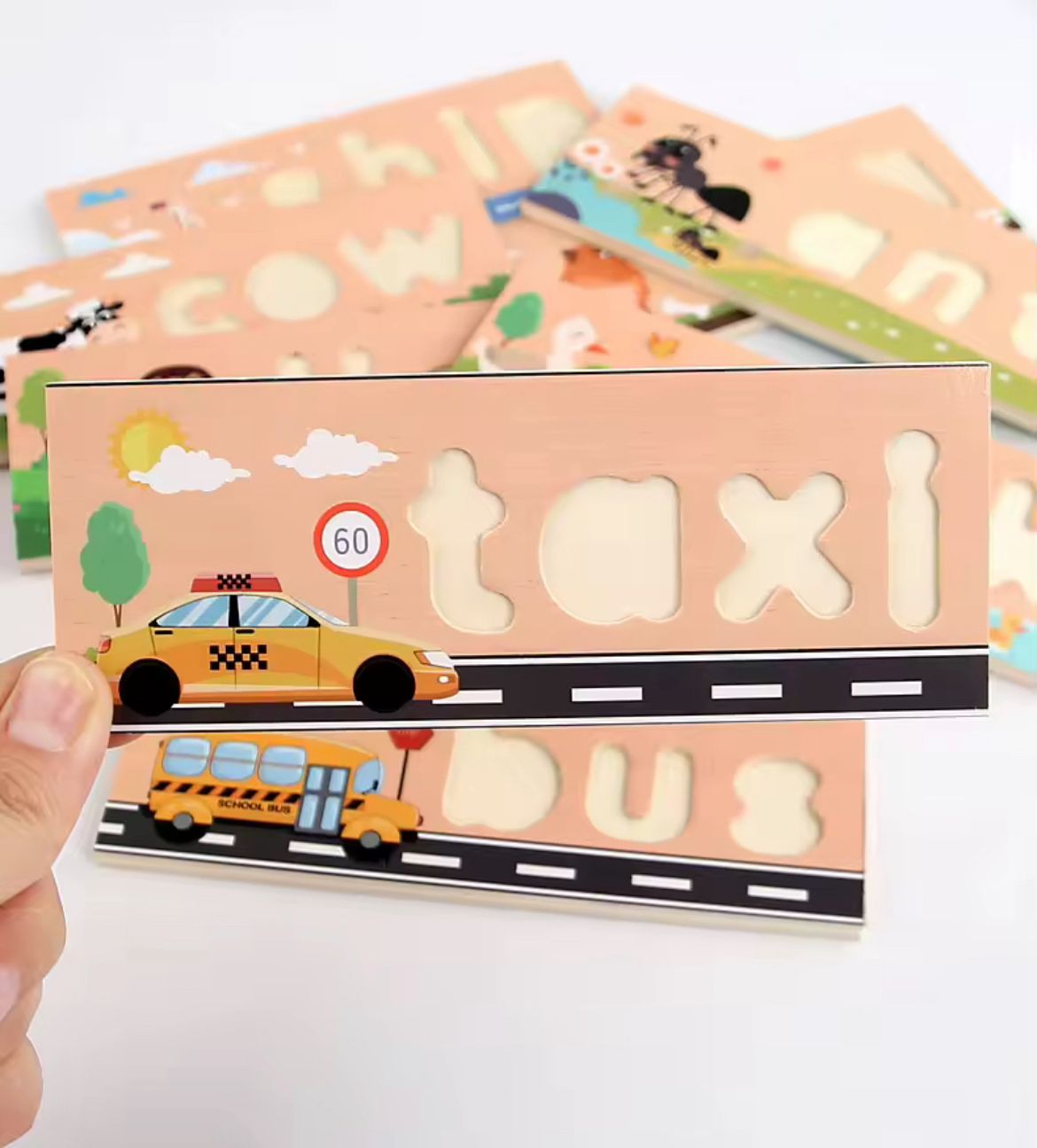 Close-up of wooden spelling puzzle board featuring the word taxi with letter cutouts and illustrated background