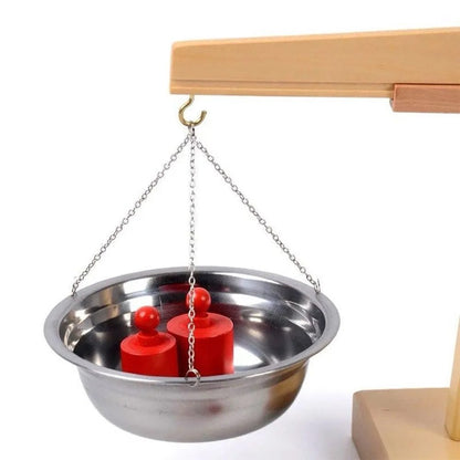 Close-up of metal pan with red weights hanging from the Montessori balancing scale.
