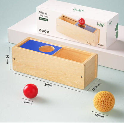 Product information view of a Montessori wooden object permanence box with sliding lid, showing dimensions and sensory balls for developing object permanence, problem-solving, and fine motor skills in young children.