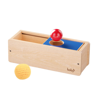 Montessori wooden object permanence box with sliding lid and sensory balls, designed to develop object permanence, fine motor skills, hand-eye coordination, and early cognitive development for babies and toddlers.